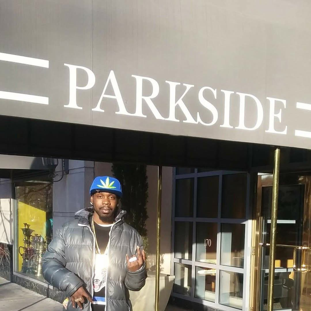 Blizz McKane con gorra azul y chaqueta acolchada, frente a la entrada de un edificio