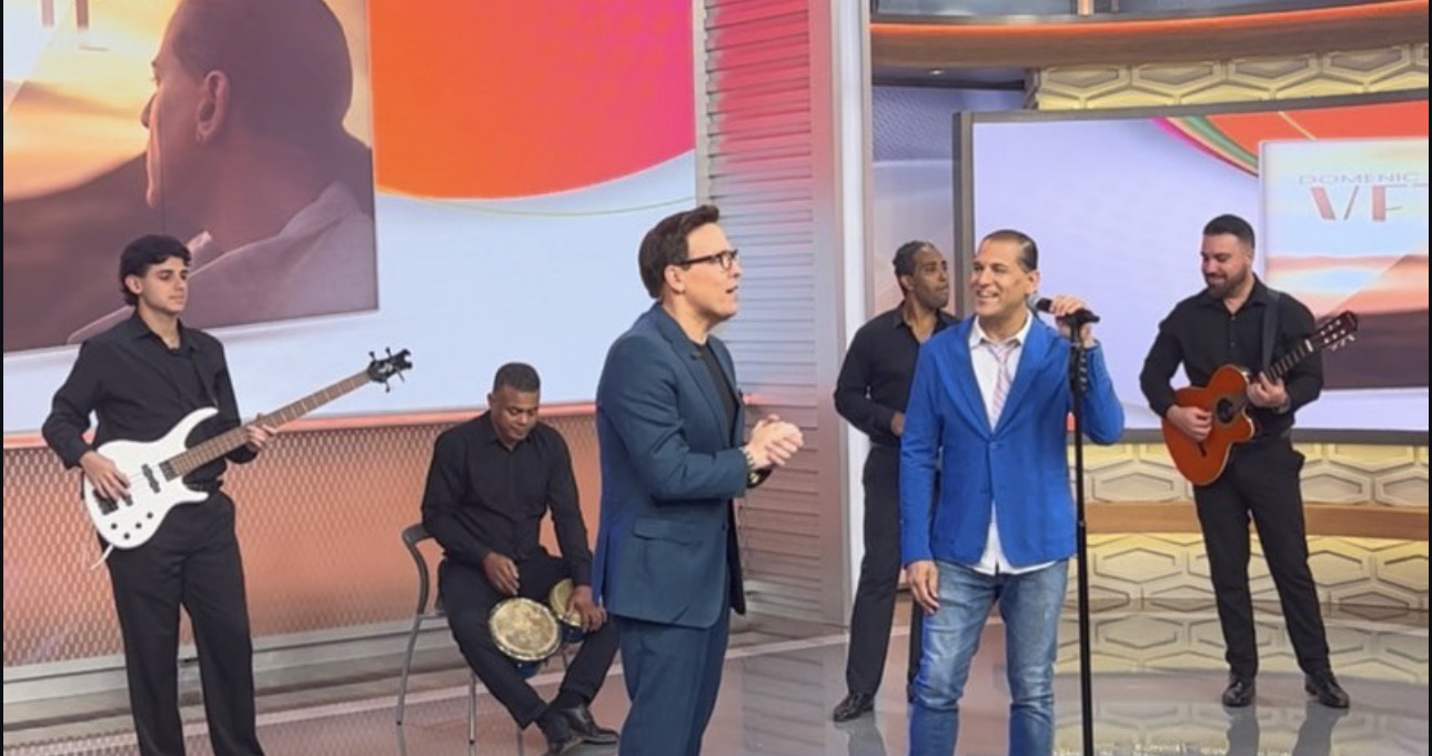 Domenic Marte cantando en un set de televisión, con su banda y un presentador