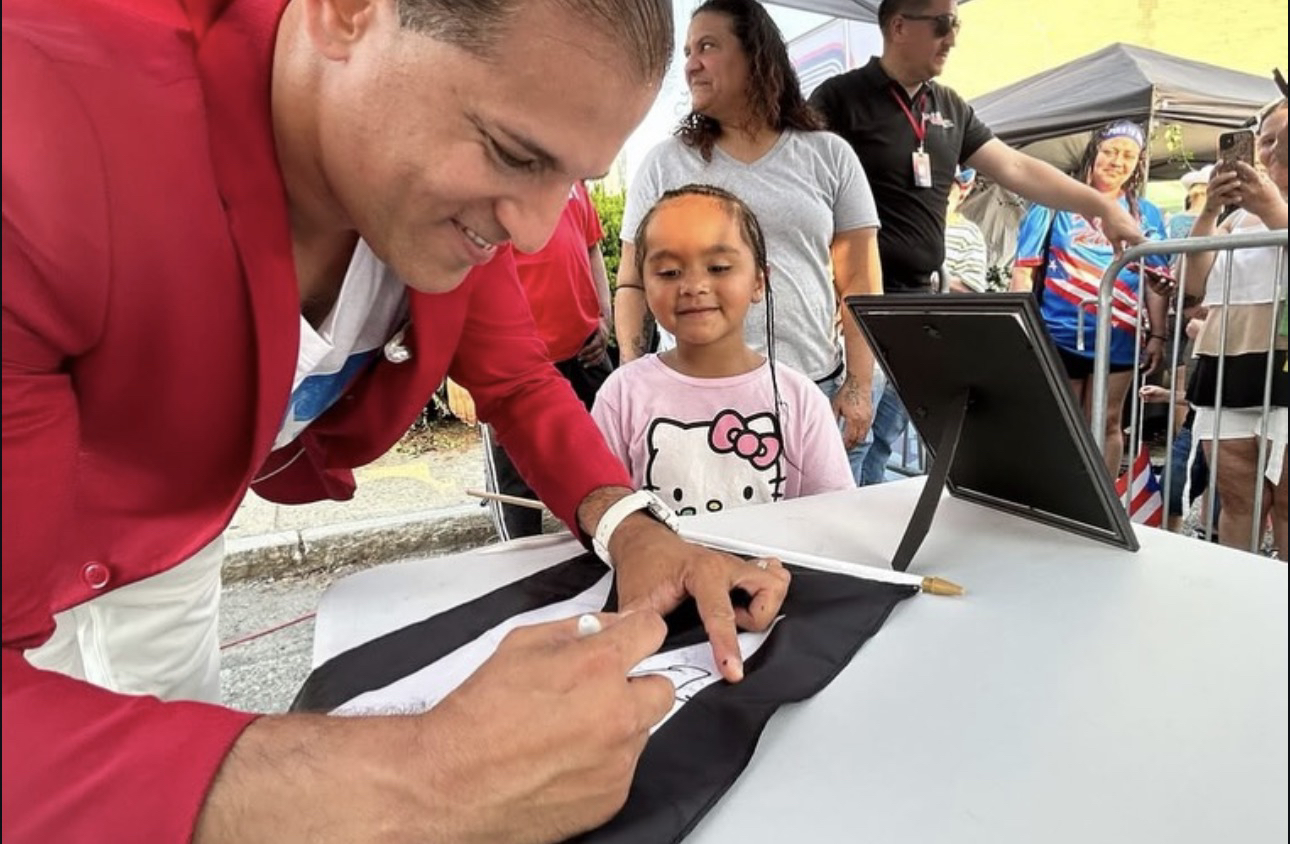 Domenic Marte firmando una bandera en un evento al aire libre