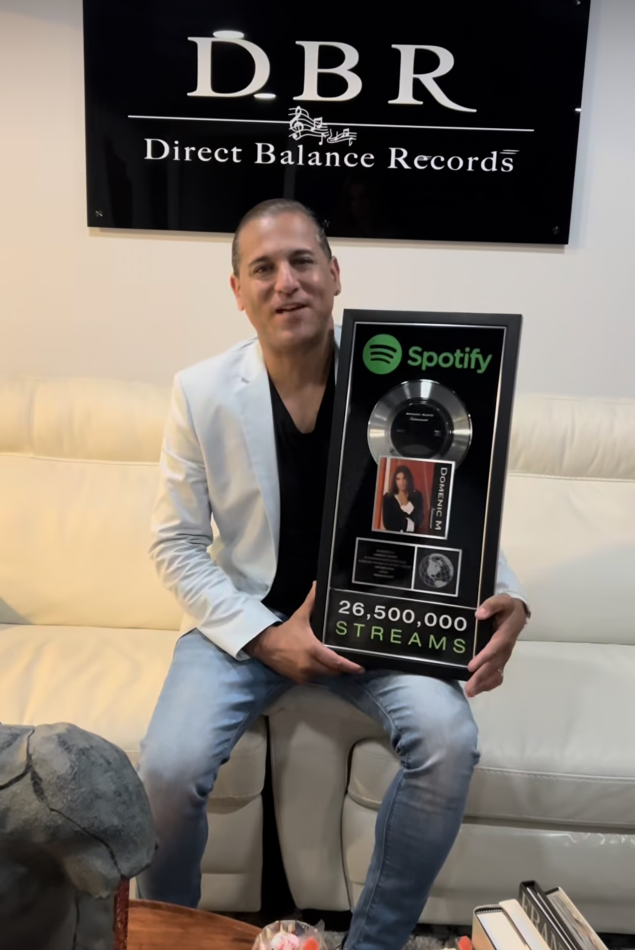 Domenic Marte sosteniendo una placa conmemorativa de Spotify, bajo un letrero de Direct Balance Records