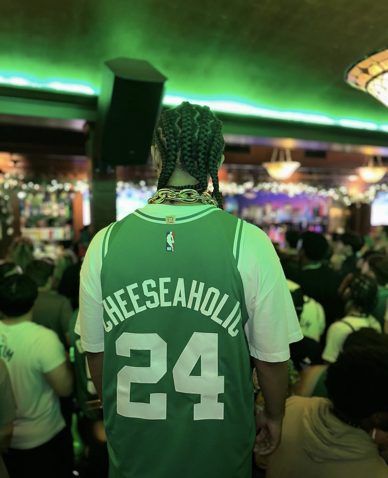 Cheeseaholic visto de espaldas, con una camiseta verde que dice CHEESEAHOLIC 24