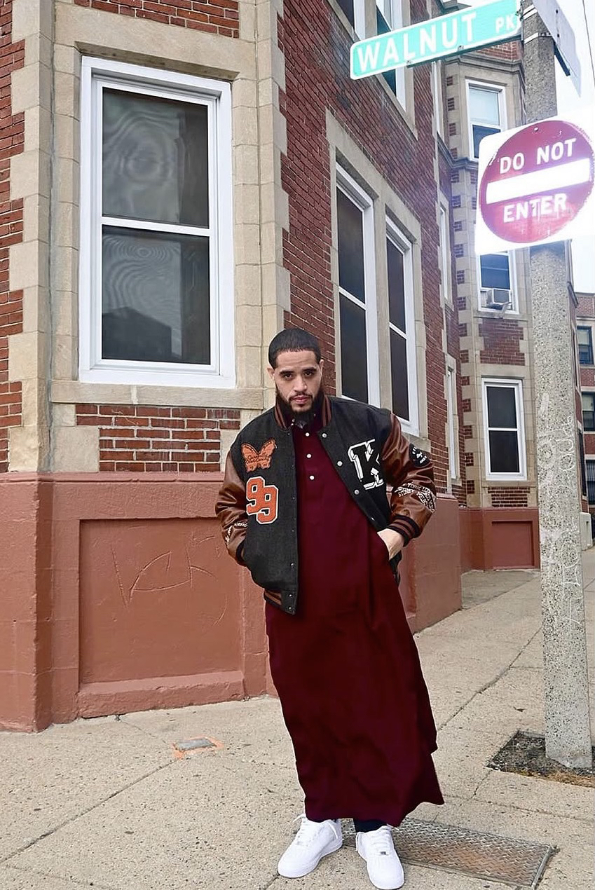 JDMilitant standing at a brick corner, in a varsity jacket