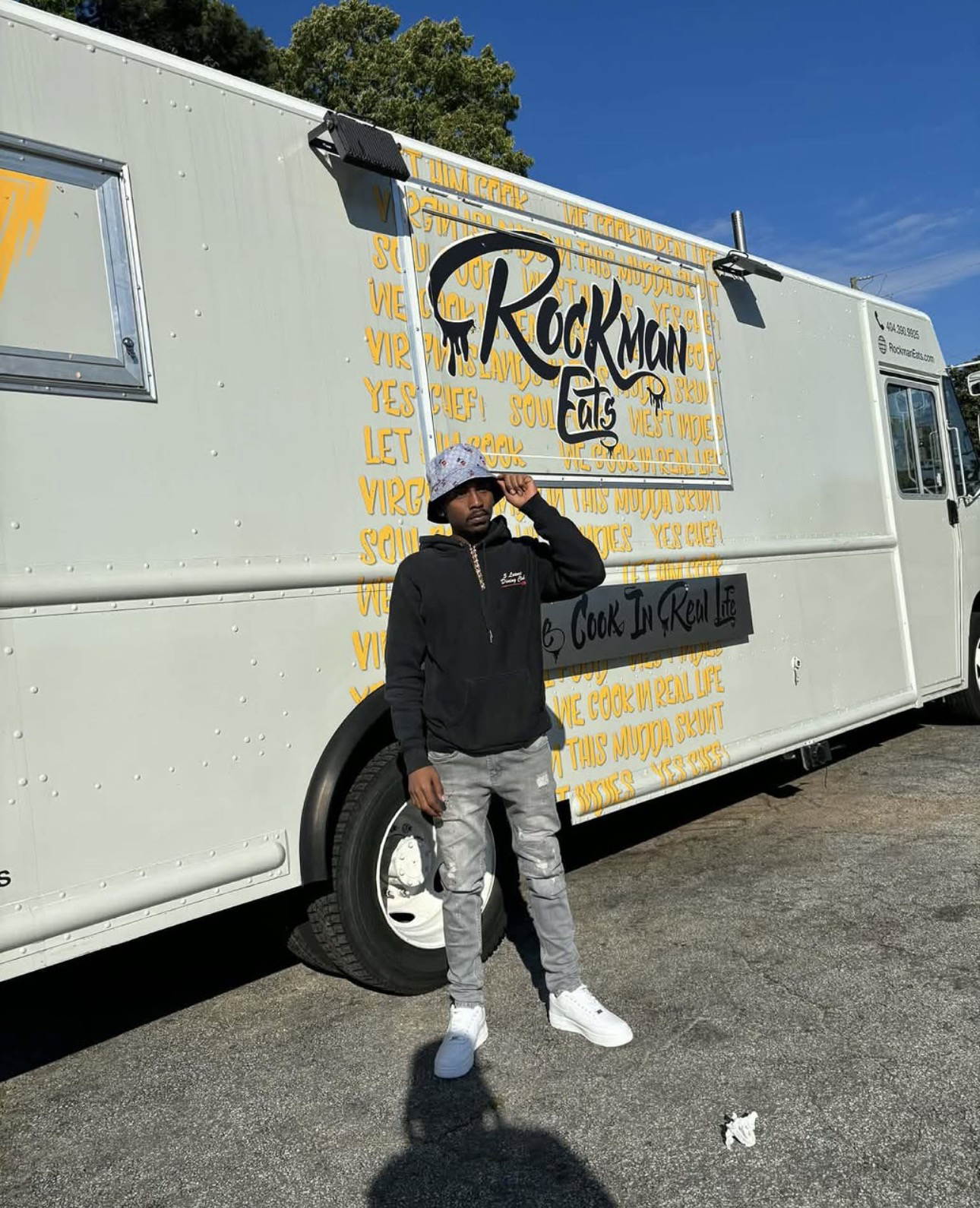 KDOT LMG de pie con un sombrero de pescador, junto a un camión de comida