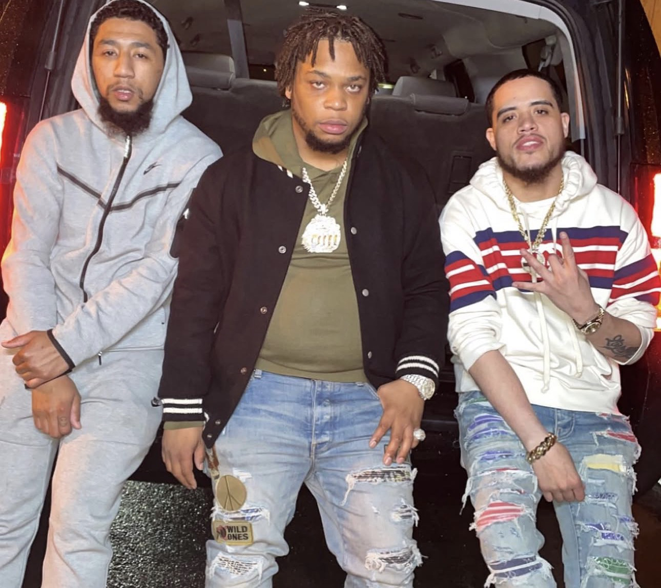 Three men posing in front of an open vehicle door, at night