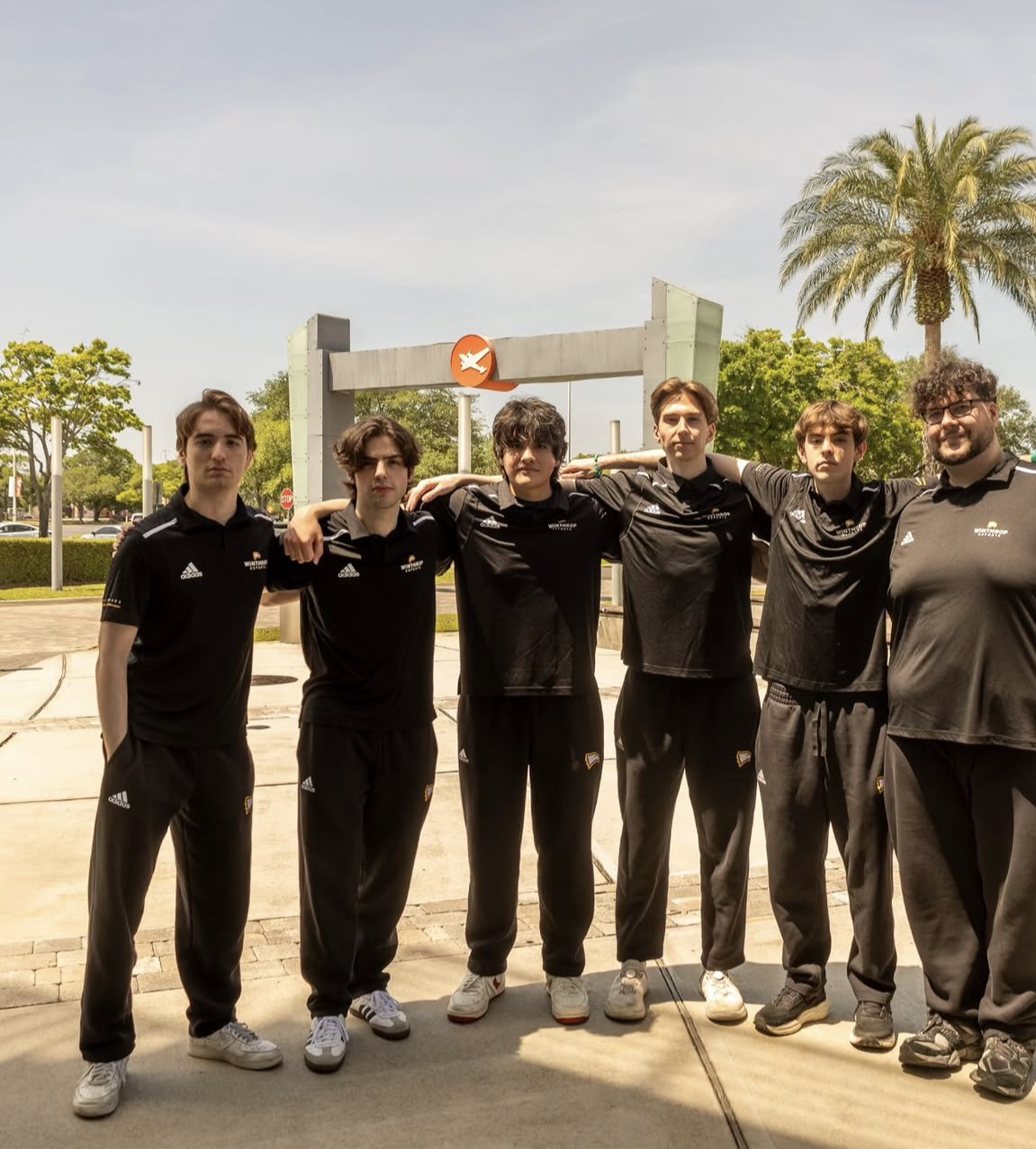 Seis jugadores abrazados al aire libre, con ropa deportiva negra