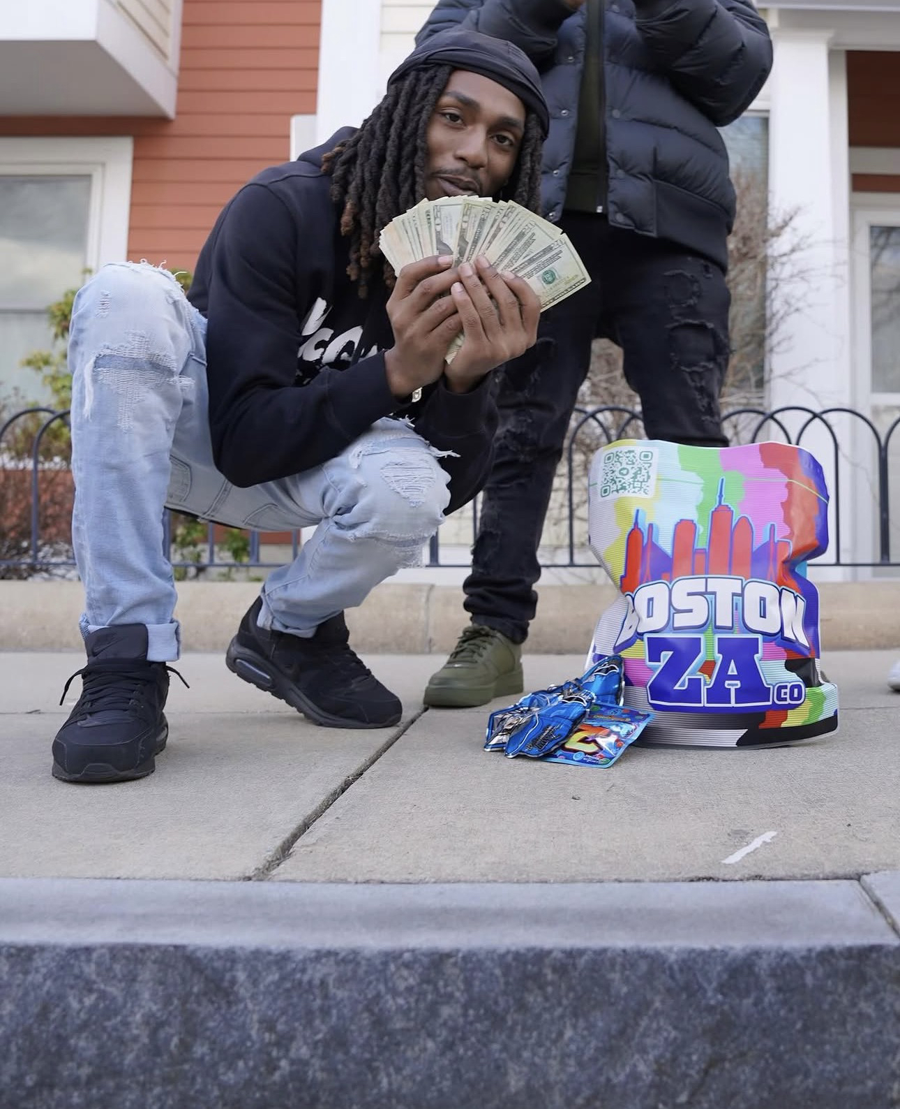 KDOT LMG agachado frente a una casa, con una persona de pie detrás