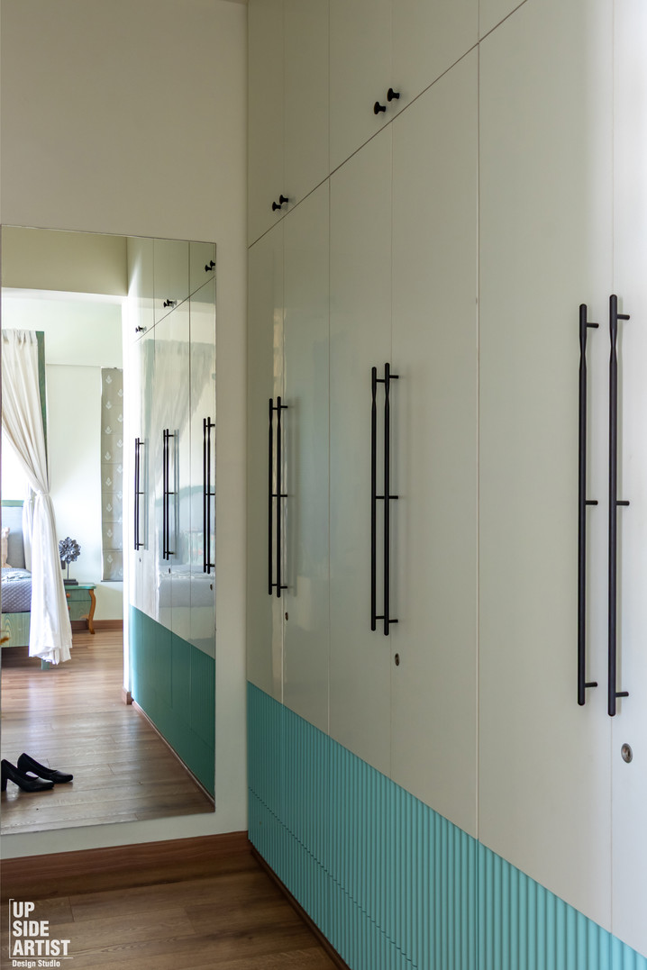 Built-in bedroom wardrobes with white doors, long vertical black handles, a fluted teal lower trim, and a mirror reflecting a canopy bed.