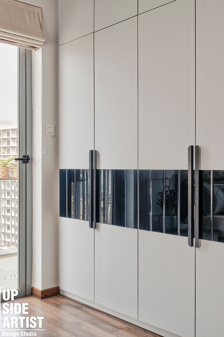 A space-saving bedroom wardrobe solution featuring seamless handleless high-gloss white cabinet doors detailed with a horizontal stripe of reflective black tinted glass and long matte black handles.