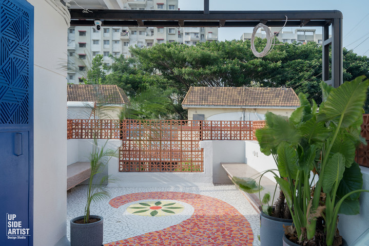 An open rooftop terrace garden featuring terracotta privacy blocks, built-in concrete benches, and a colourful mosaic floor art pattern.