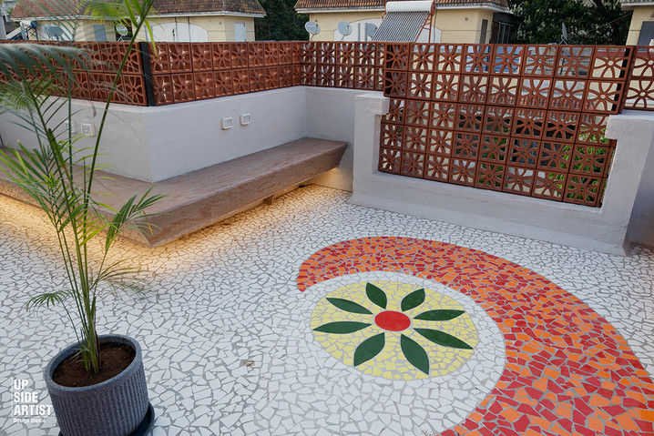 Close-up of a decorative yellow, green, and orange broken tile mosaic floral pattern on a white outdoor terrace floor.