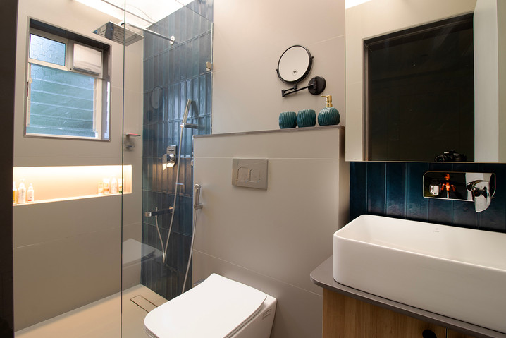 Contemporary bathroom featuring a white vessel sink on a wooden cabinet, a wall-mounted toilet, a magnifying mirror, and a glass walk-in shower with vertical blue tiles and a backlit niche.