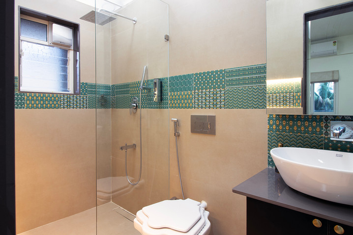Close-up of a long, recessed horizontal shower shelf with blue and green patterned mosaic tiles, illuminated by hidden warm LED strip lighting and holding soap dispensers.
