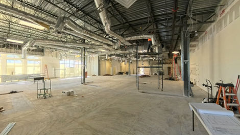 Construction photo of front retail space during demo with exposed ceiling ducts and unfinished flooring.