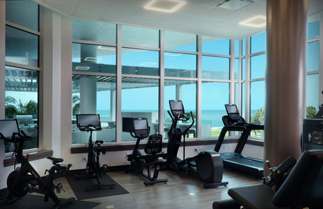 Cardio workout area featuring Peloton bikes, ellipticals, and treadmills with panoramic ocean views at Regent Condominium Fitness Center.