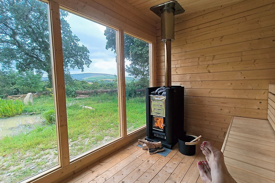 Relaxing in the wood-fired sauna at with epic view of the Pembrokeshire National Park at Top of the Woods. A luxury eco glamping holiday retreat for nature-based and slow-travel stays in Wales.