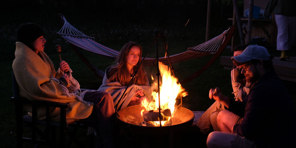 Friends gathered around a campfire at Top of the Woods in Pembrokeshire, wrapped in blankets and enjoying a relaxed evening outdoors. A cosy nature-based holiday experience with wildlife, dark skies, campfires and time to reconnect in the Welsh countryside.
