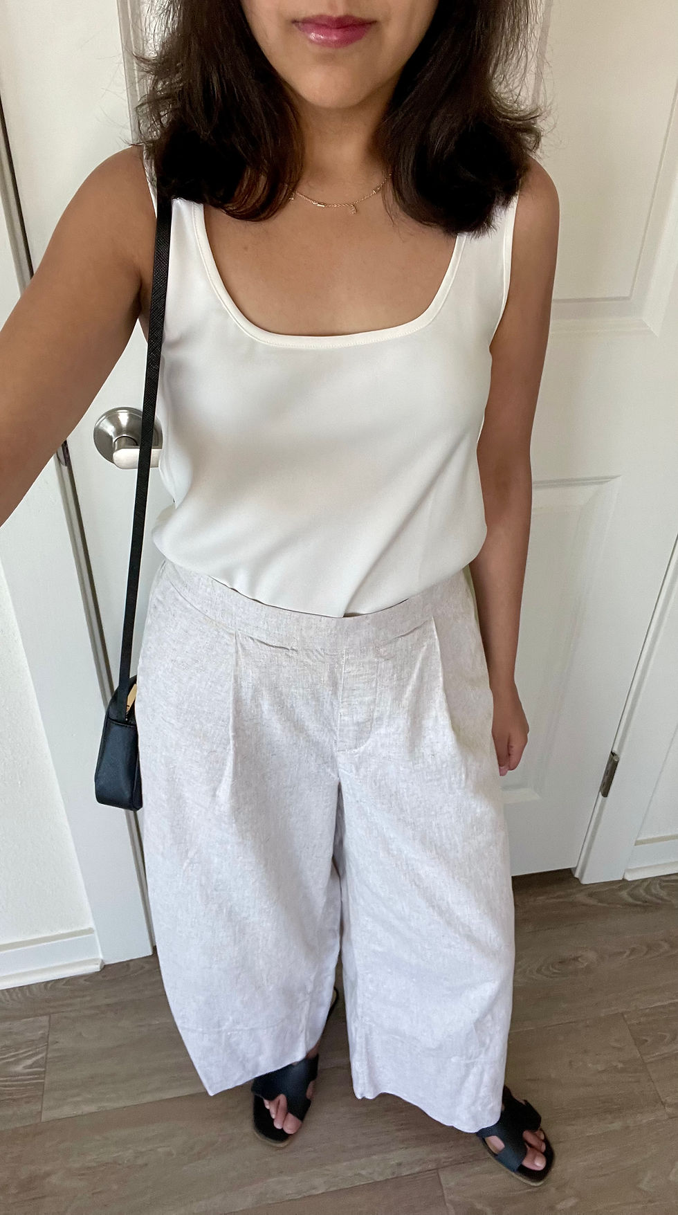 White satin tank top, light beige linen pants, baguette necklace, black sandals, and black crossbody bag
