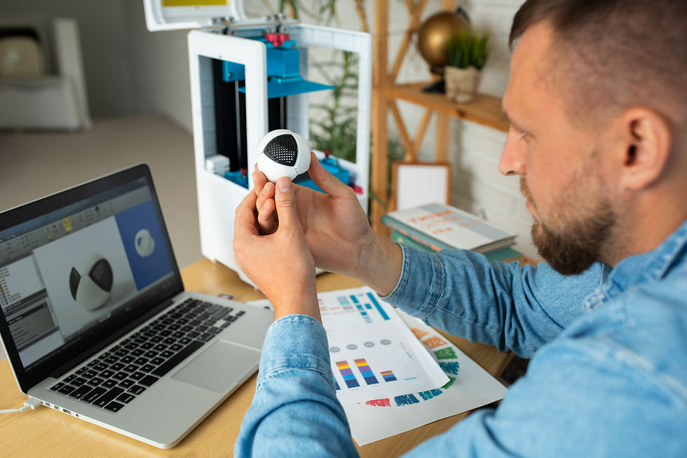 A designer working with a 3D printed object in hand while analyzing the design on a laptop screen, with a 3D printer in the background.