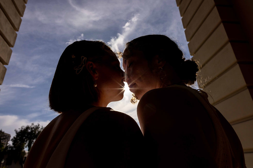 Two people silhouetted against a bright sky, close together with a sun flare between them. The mood is intimate and serene.