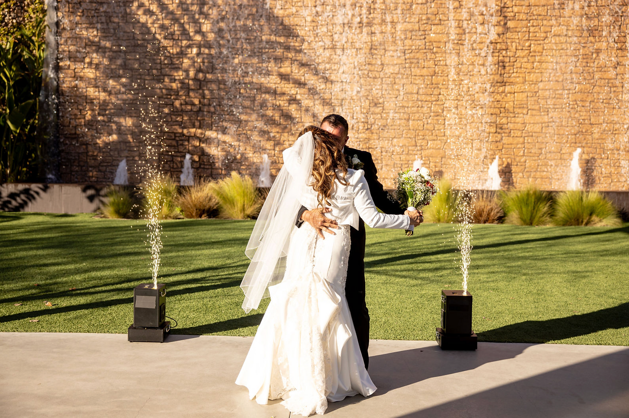 Bride and groom embracing at outdoor wedding with waterfall