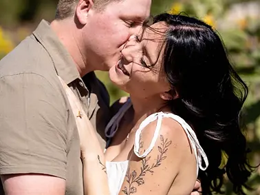couple kissing outside in a sunflower field during their engagement session she is wearing