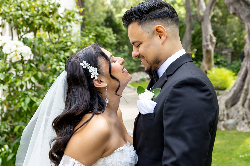 Thursday Club La Canada First Look on wedding day. A smiling bride and groom gaze at each other in a garden. She wears a white dress and veil; he wears a black suit. Lush greenery surrounds them.