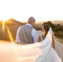 Wedding couple walking into a bright sunset with a flowing veil.