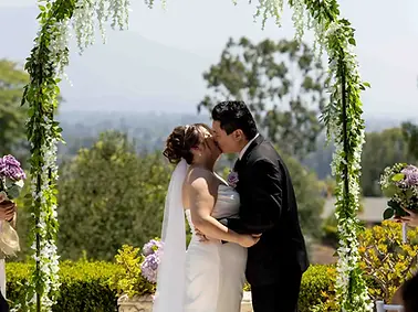 Bride and groom share their first kiss under a greenery arch at a backyard wedding in Pasadena.