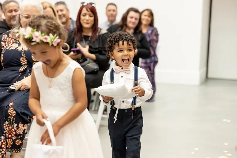 flower girl and ring bearer cannot stop laughing as they walk into wedding ceremony