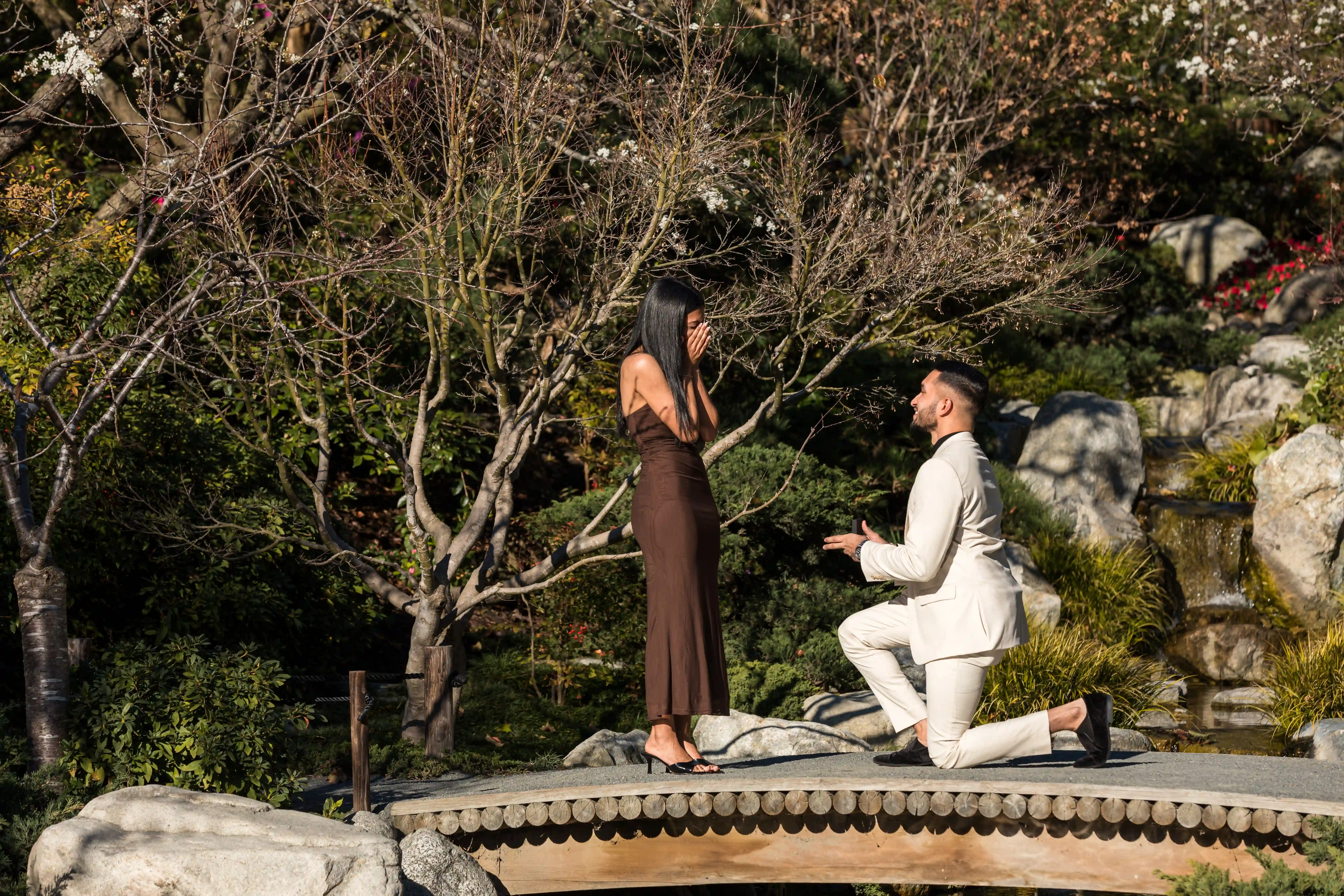 Man kneels on bridge proposing to woman