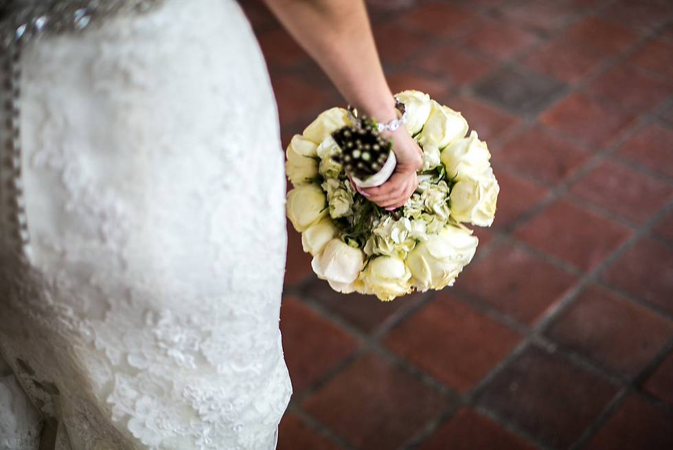 Brides in lace dress holding white rose bouquet, standing on red tiled floor. Elegant and serene setting.