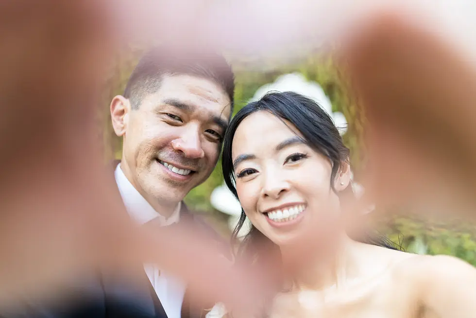 couple holding their hands together to make a heart as they smile behind it