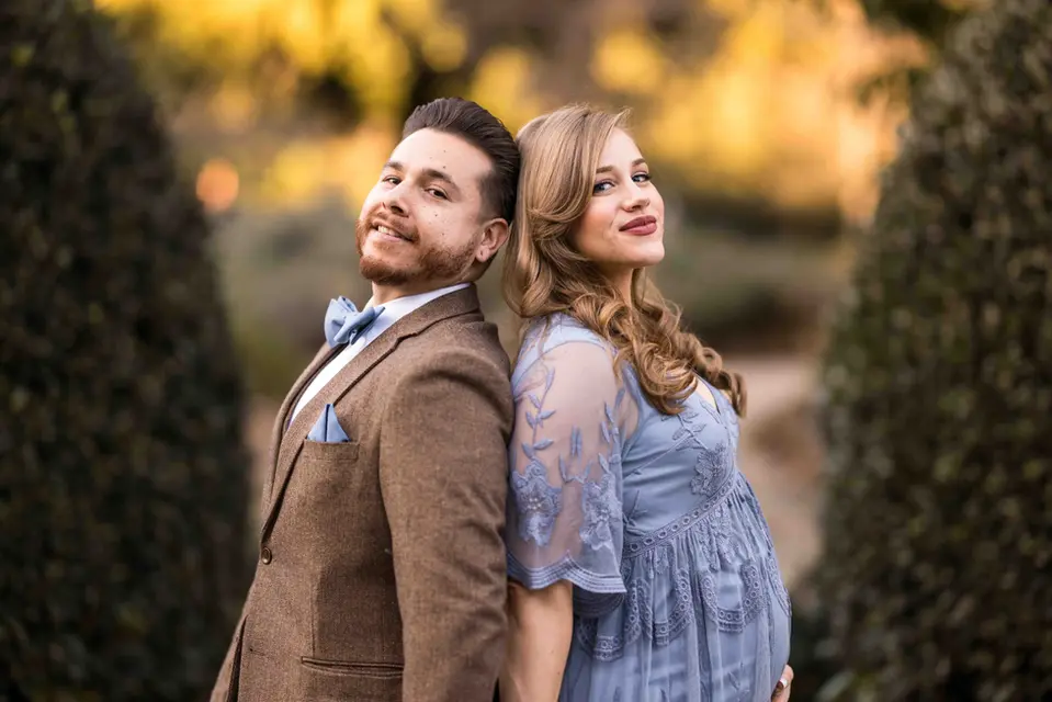 couple maternity pregnancy photos.  They stand back to back looking at the camera.  She wears a blue dress