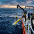 Crew on research boat deploys a yellow ocean sensor at sunset over rough seas.