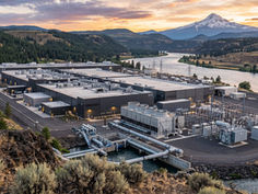 Industrial power plant by a river at sunset, with snowcapped mountain, forested hills, and visible U-4 markings.