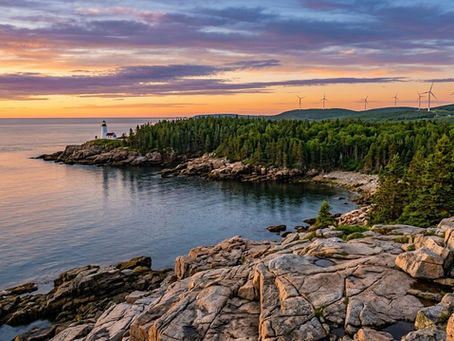 Sunset over rocky forested coast with a lighthouse, calm water, and wind turbines on distant hills.