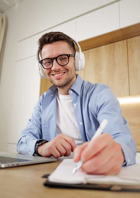 cheerful-male-student-enjoys-music-headphones-while-writing-his-planner-laptop.jpg
