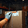 Gloved hands taping a cardboard shipping box closed with a shipping label on top, dark wor