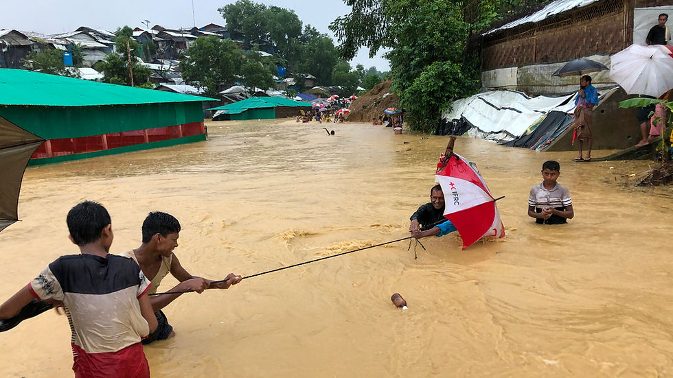 People help each other to cross a stream in Balukhali. Normally the stream is dry but monsoon rains flooded it completely in 2021. © Ro Yassin Abdumonab.