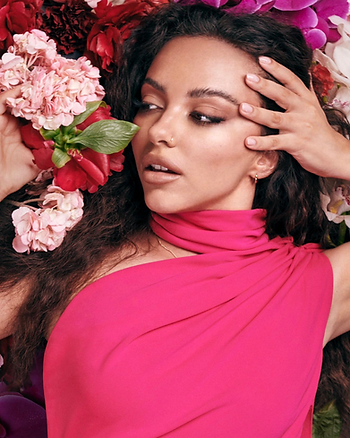 A close-up shot of Jade Thirlwall lying on a bed of pink flowers in minimal, glowy makeup for Little Mix's Between Us album art.
