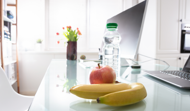 Workspace with a computer ona desk and healthy snacks - apples, bananas and water