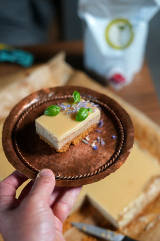 A slice of rhubarb cottage cheese cake on a copper plate with basil and corn flower petal garnish