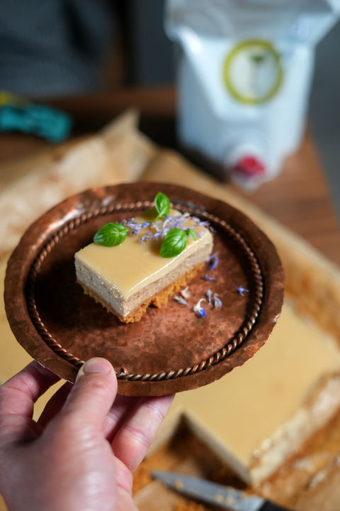 A slice of rhubarb cottage cheese cake on a copper plate with basil and corn flower petal garnish