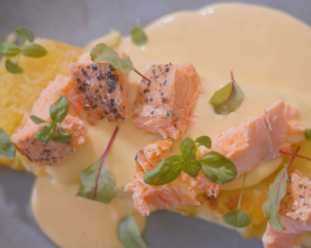 Top down view of a potato rosti or hash brown with creamy eggs draped on top, decorated with chunks of smoked salmon and microgreens