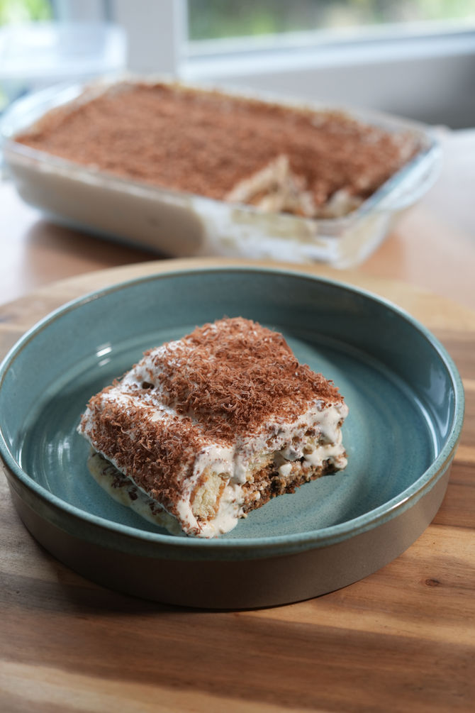 Kvassamisu, a tiramisu variation, sitting on a green plate with the rest of the kvassamisu out of focus in the background.