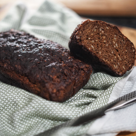 A couple of loaves of dark rye bread with sunflower seeds, on a rustic cloth. One is cut, showing the inside of the bread.