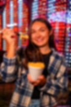 Woman holding mac and cheese in front of carnival lights.