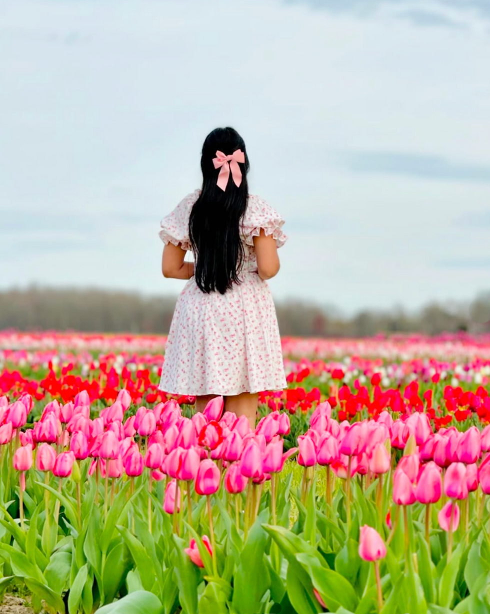 Woman with pink bow stands among vibrant pink and red tulips.