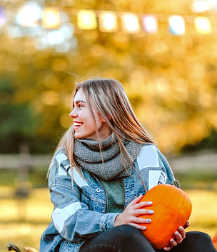A smiling young adult girl has a large smile holding a pumpkin