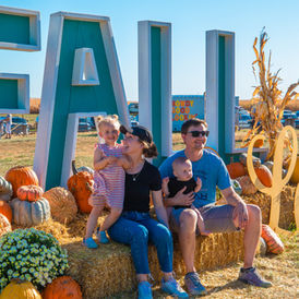 Family posing by large FALL sign with pumpkins.